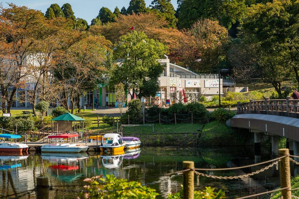 A park with a river, boats, a bridge, and trees.