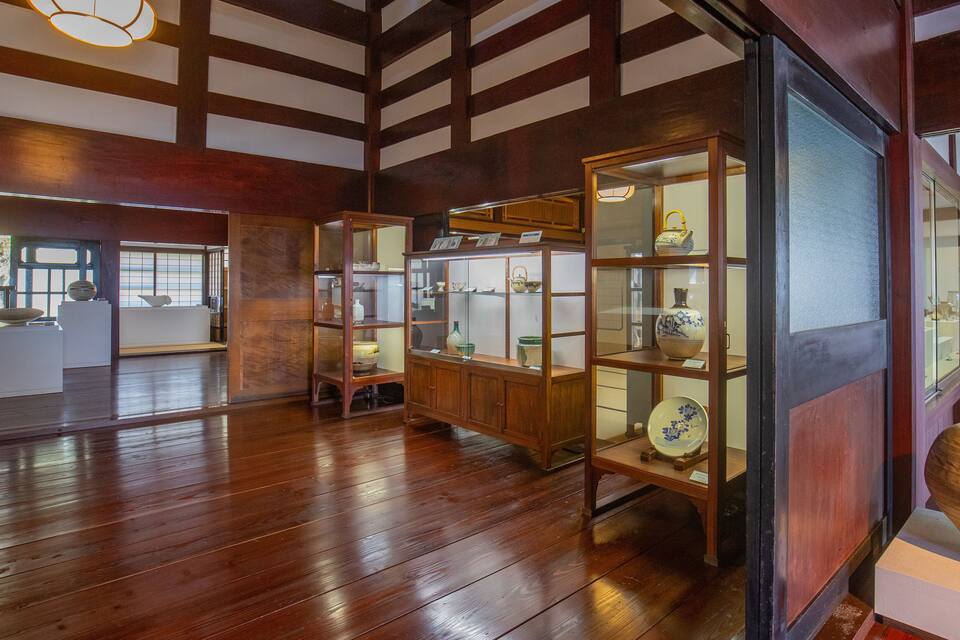 A traditional Japanese interior with wooden floors, tatami mats, and display cases of ceramics.
