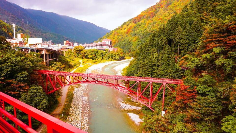A red bridge over a river, surrounded by lush greenery and mountains.