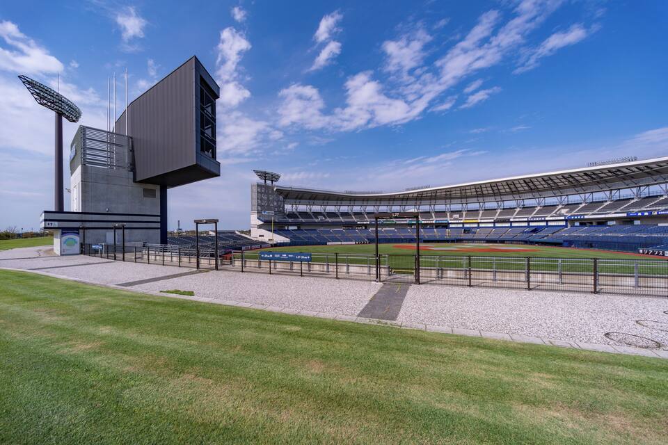 A modern baseball stadium with a large screen, seating, and a clear blue sky.