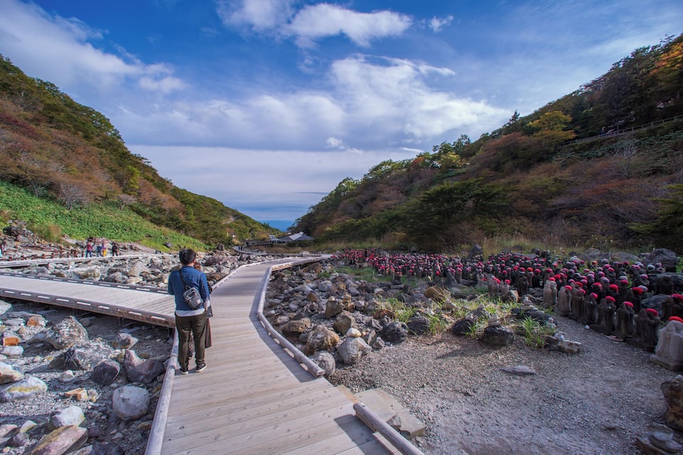 A wooden boardwalk curving through a rocky landscape with a person walking.