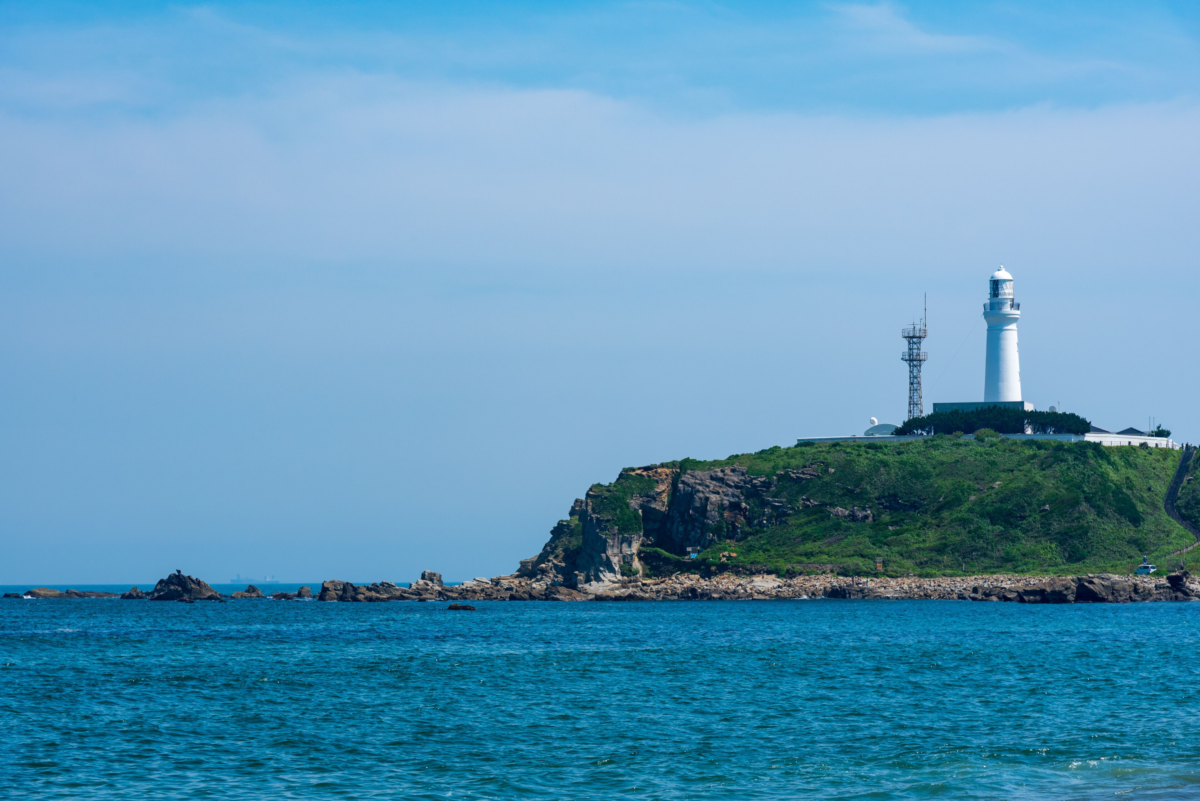 A lighthouse on a green cliff by the sea.