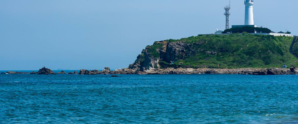 A lighthouse on a green cliff by the sea.