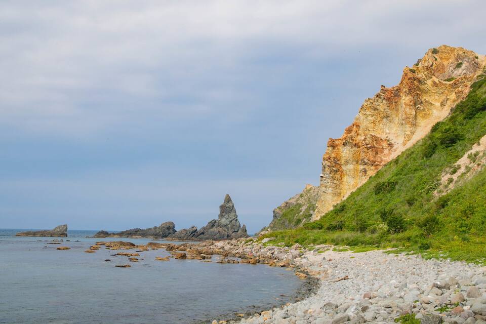 Costa rochosa com um penhasco imponente e uma pequena ilha rochosa ao longe.