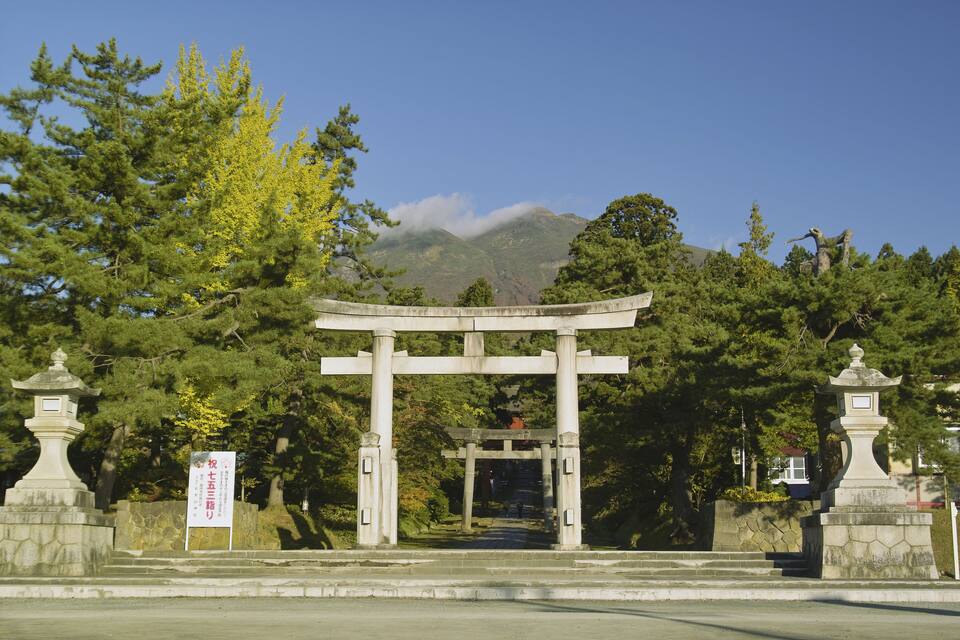 A traditional torii gate at the entrance of a shrine surrounded by lush greenery and a mountain in the background.