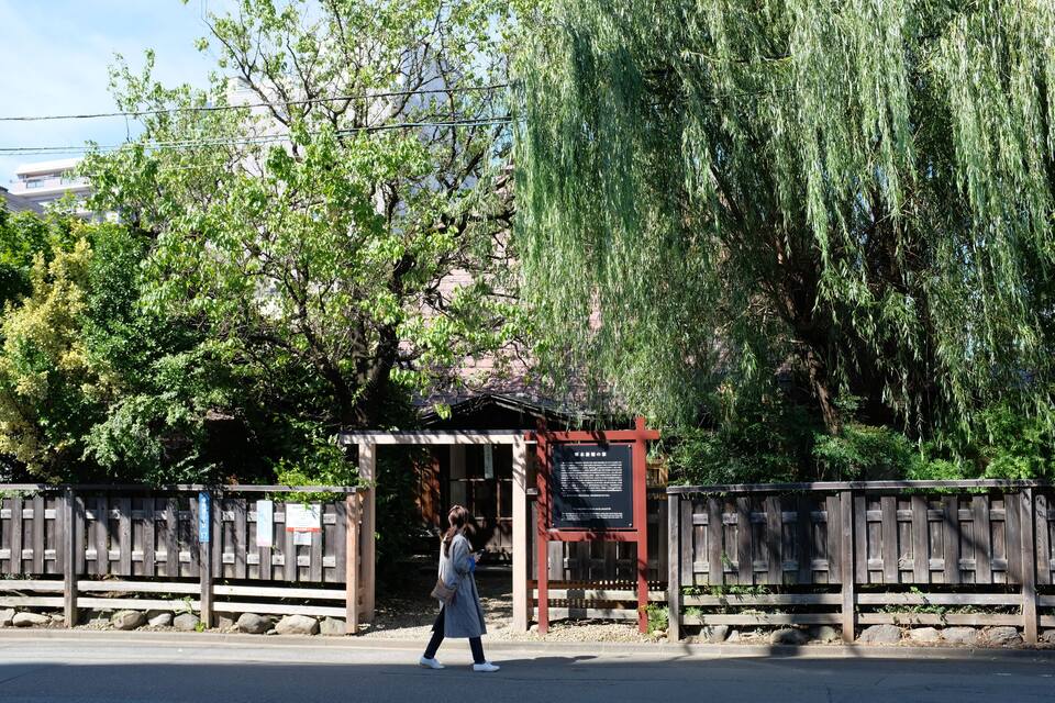 A pedestrian crossing a street with a wooden fence and a signboard.