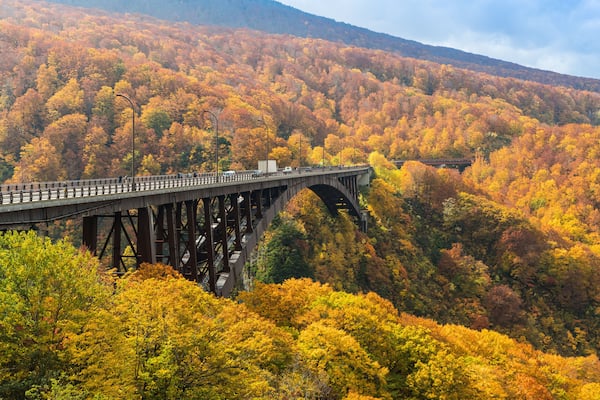 Un pont d’acier enjambant une vallée, avec le feuillage automnal qui l’orne.
