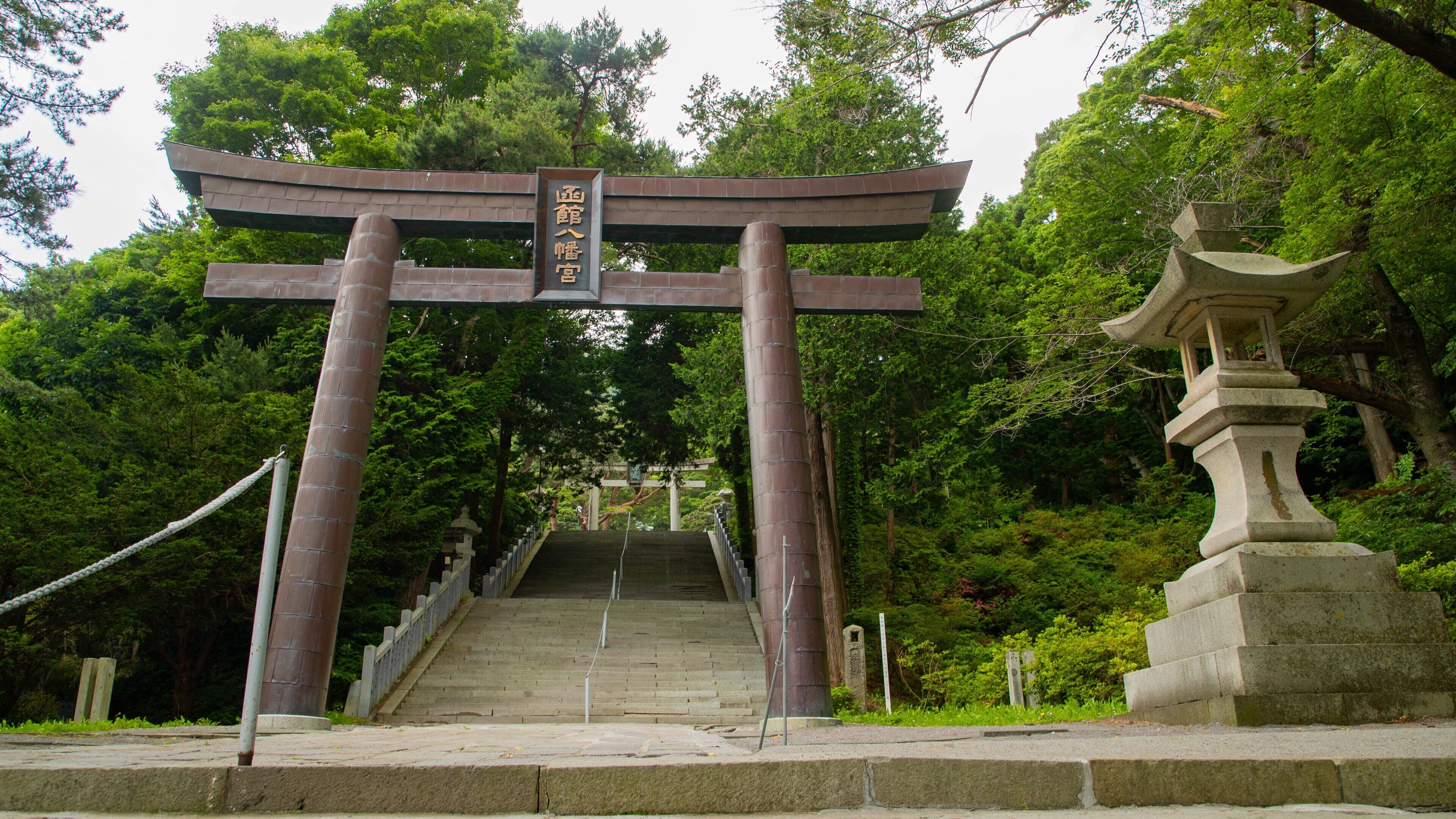 A traditional Japanese torii gate leading up a stone staircase surrounded by lush greenery.