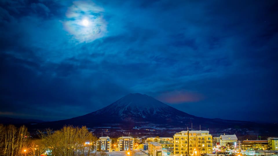 A snow-covered mountain at night with a lit town in the foreground.