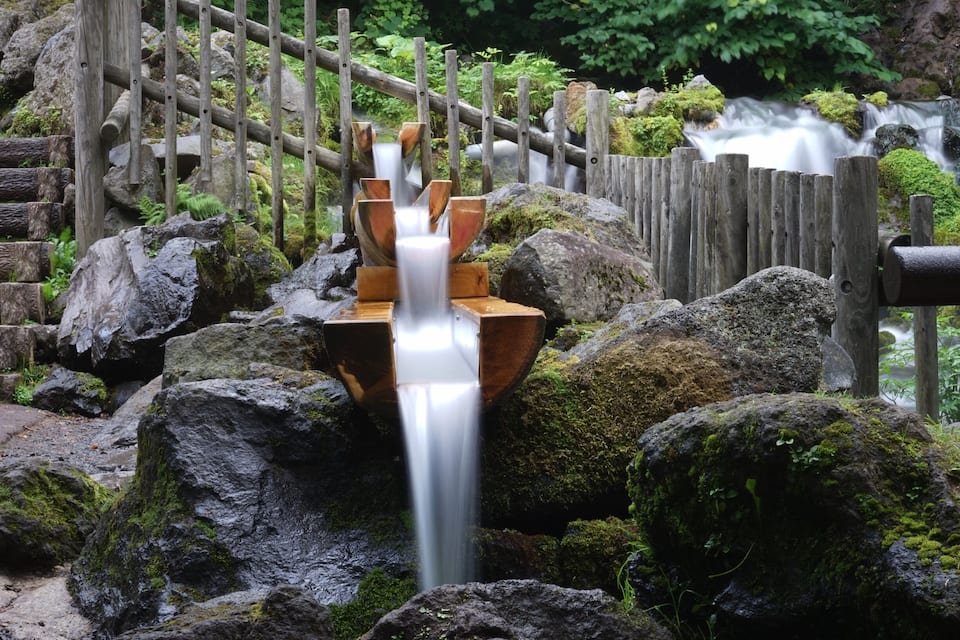 A wooden fence, a waterfall, and moss-covered rocks.