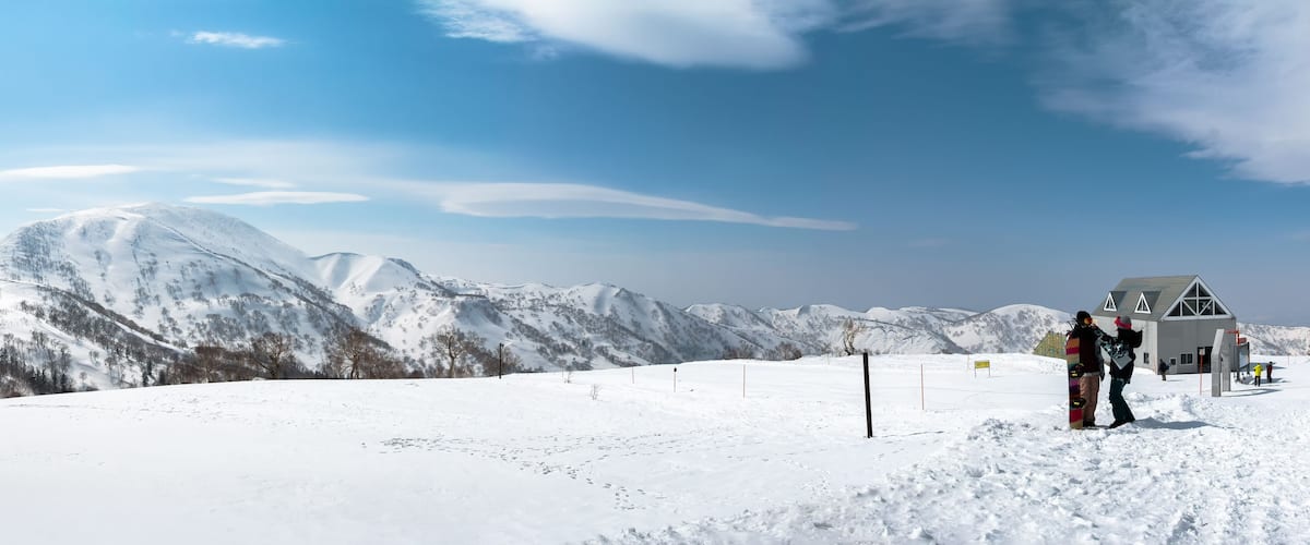 A snowy mountain landscape with a ski lift and a building in the background.