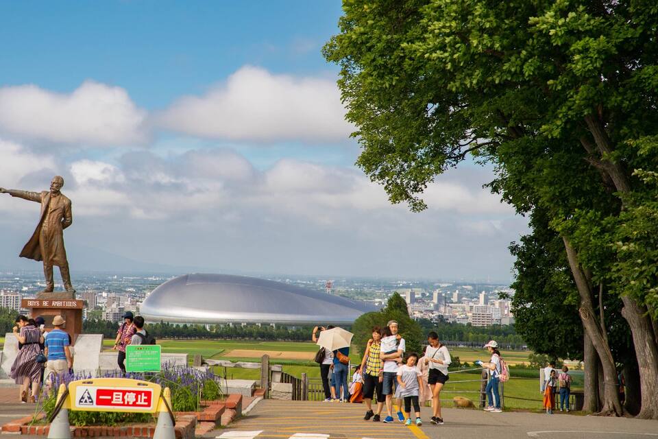En staty av en man som pekar åt vänster, en stor stadion och en park med folk i.
