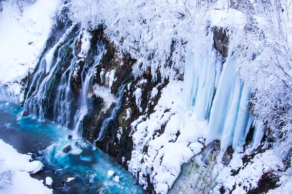 Uma cascata congelada com icículas e árvores cobertas de neve.