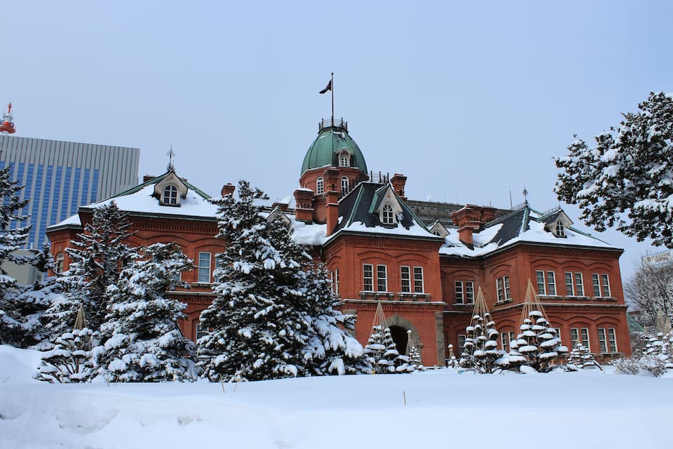 A large red brick building with a green dome and snow-covered trees.