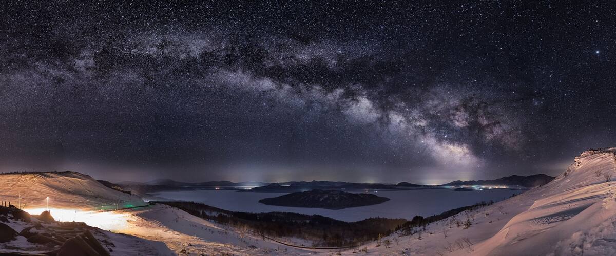 A starry night sky over a snowy landscape with a lake and mountains.