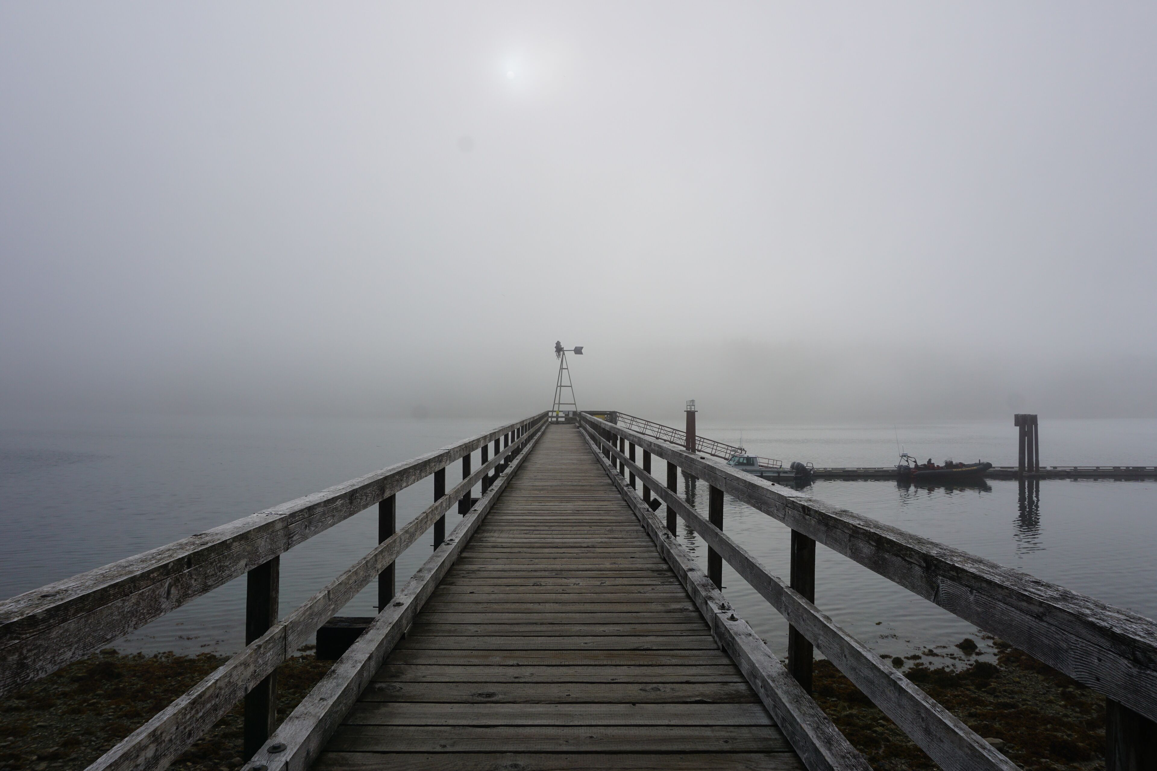 A wooden pier extending into a foggy body of water with a lighthouse in the distance.