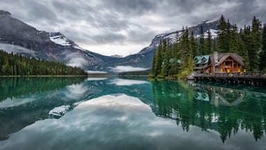 Un lago de montaña con una cabaña y bosque.