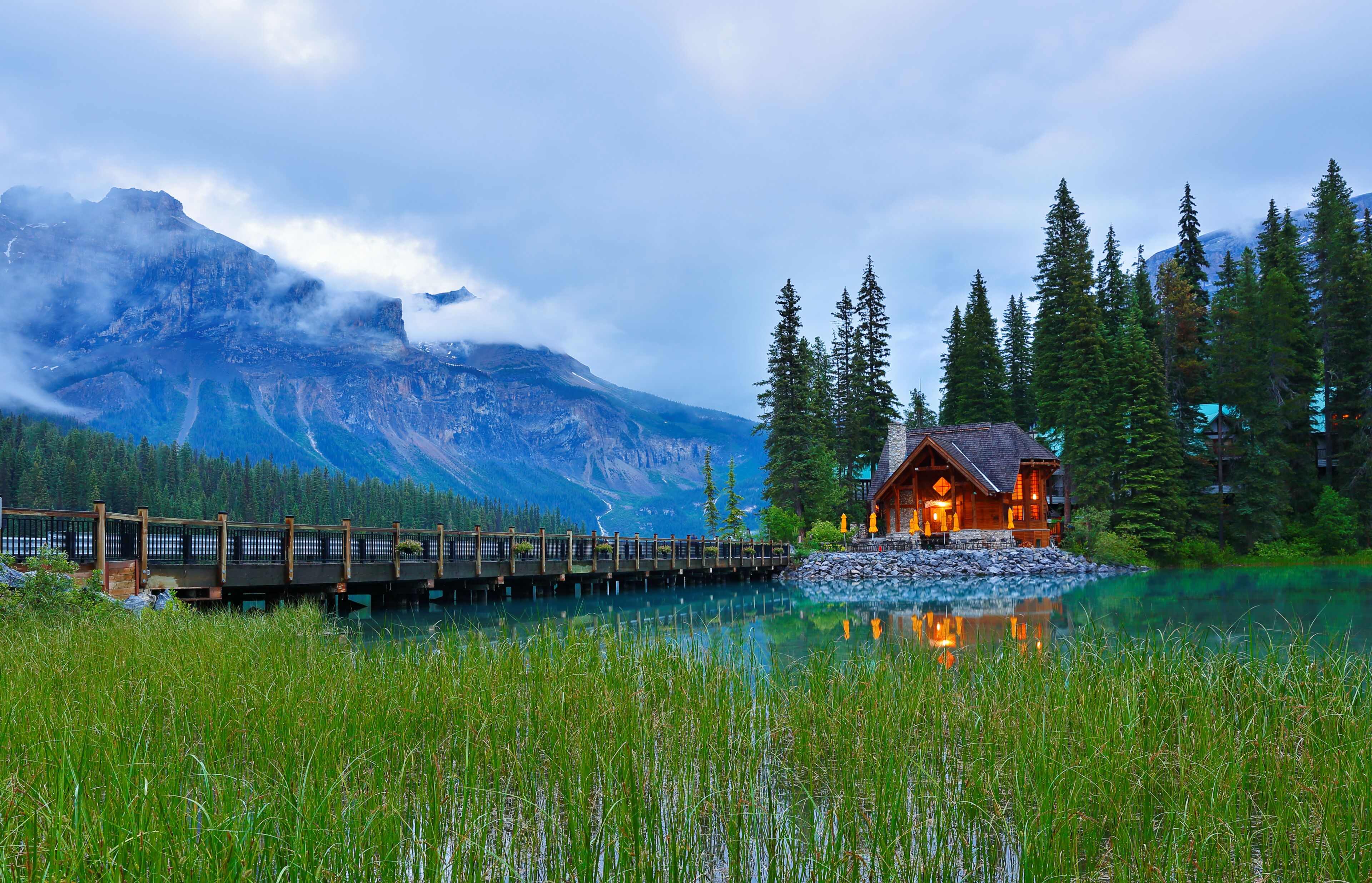 A wooden bridge over a lake, a cabin, and a mountain range.