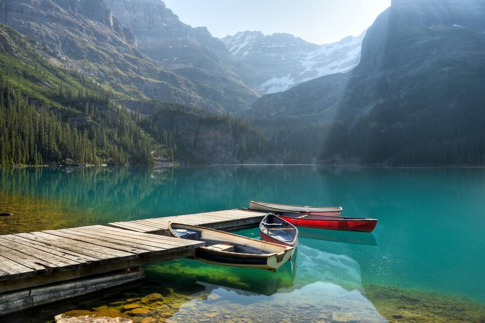 A calm lake with clear turquoise water, surrounded by dense green forests and mountains.