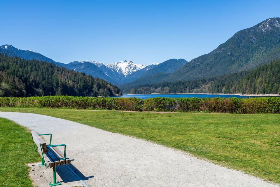 A gravel path leading to a bench overlooking a lake with mountains in the background.