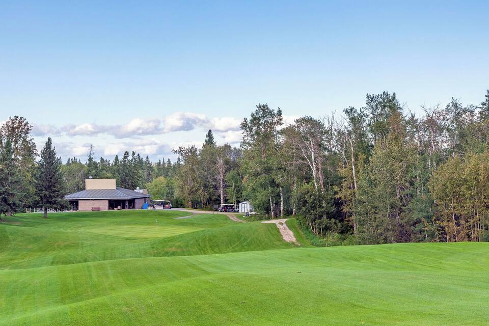 A golf course with a clubhouse, a clear sky, and a forested area.