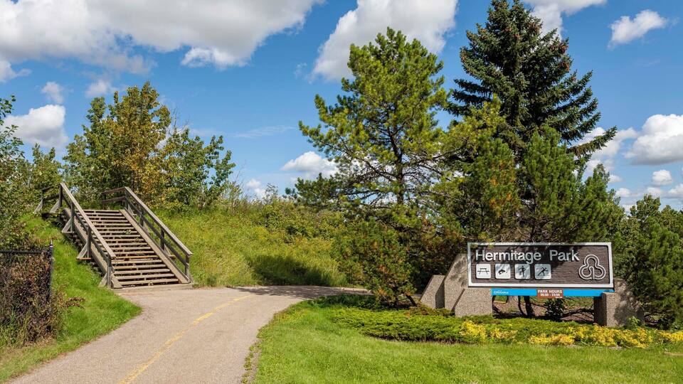 A sign for Hermitage Park with a wooden staircase leading up to a road.