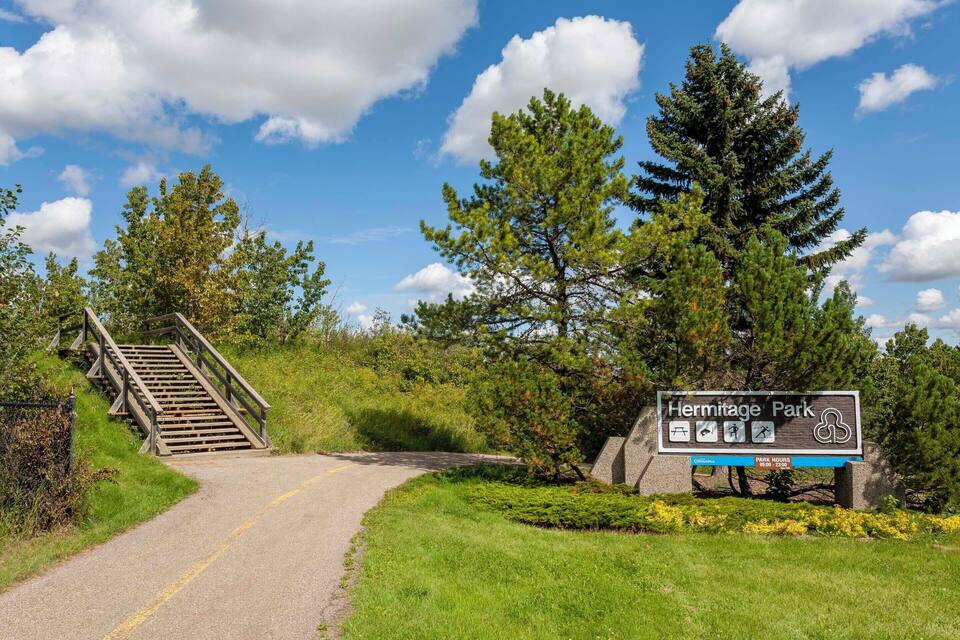 A sign for Hermitage Park with a wooden staircase leading up to a road.