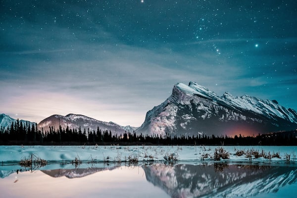 Une chaîne de montagnes enneigées au crépuscule, se reflétant clairement dans un lac paisible.