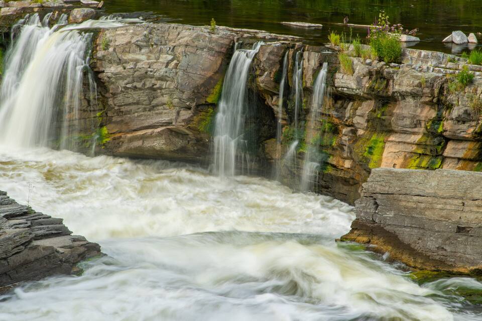 A multi-tiered waterfall cascading over rocky terrain with lush greenery and a calm pool below.