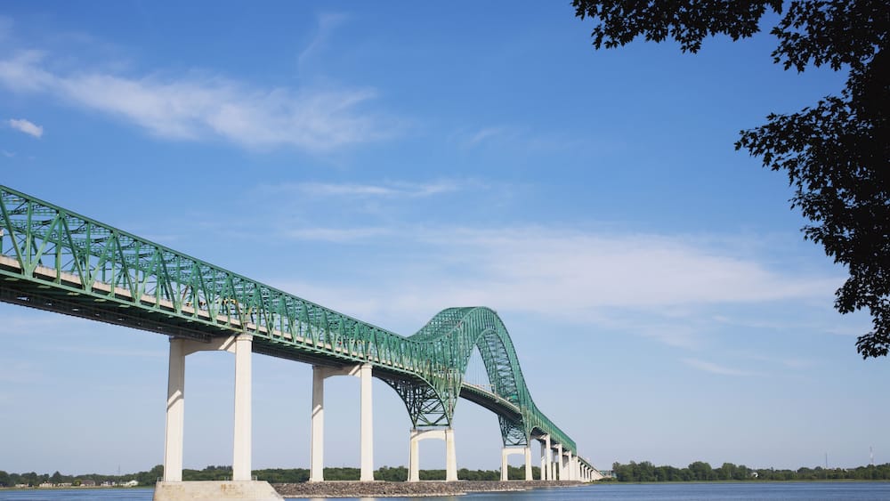 Eine große grüne Brücke überspannt einen Fluss, bewölkter, klarer Himmel.