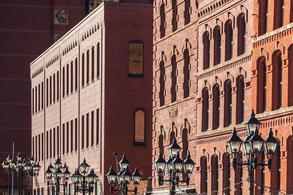 A row of red brick buildings with arched windows and street lamps.