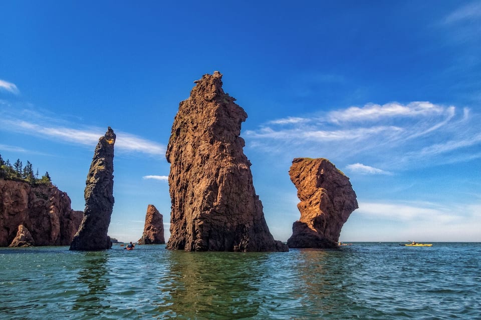 Paesaggio costiero con imponenti formazioni rocciose e kayakisti in acqua.
