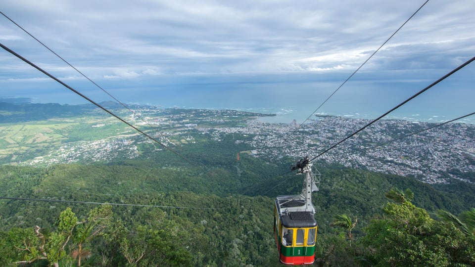 A cable car over a lush green landscape with a city in the distance.