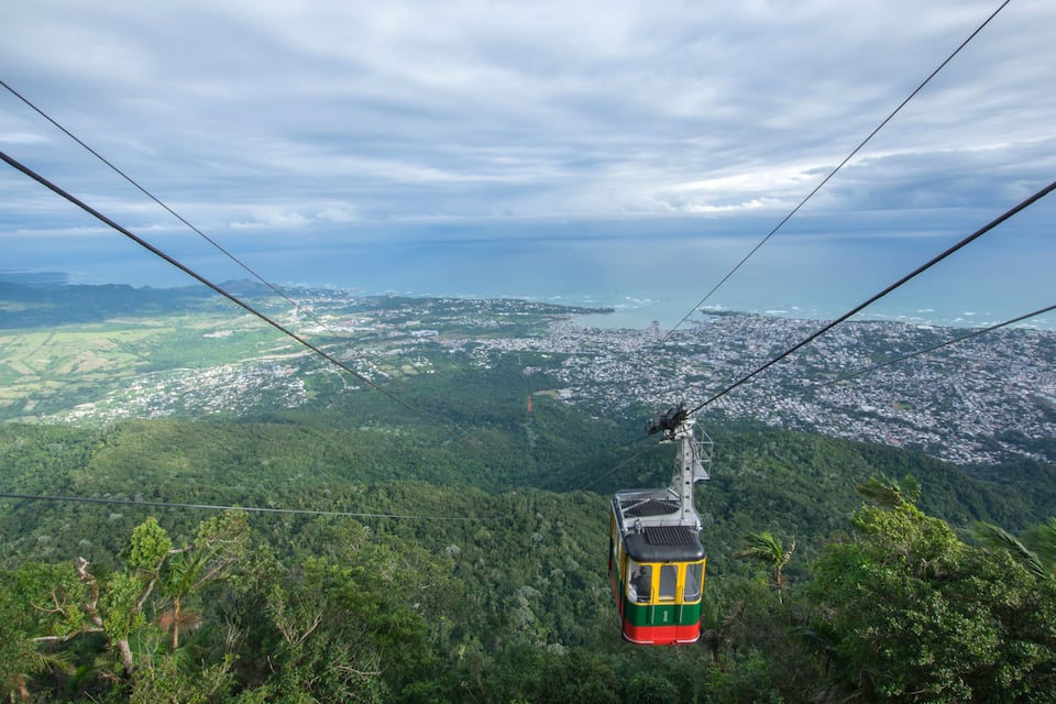 A cable car over a lush green landscape with a city in the distance.