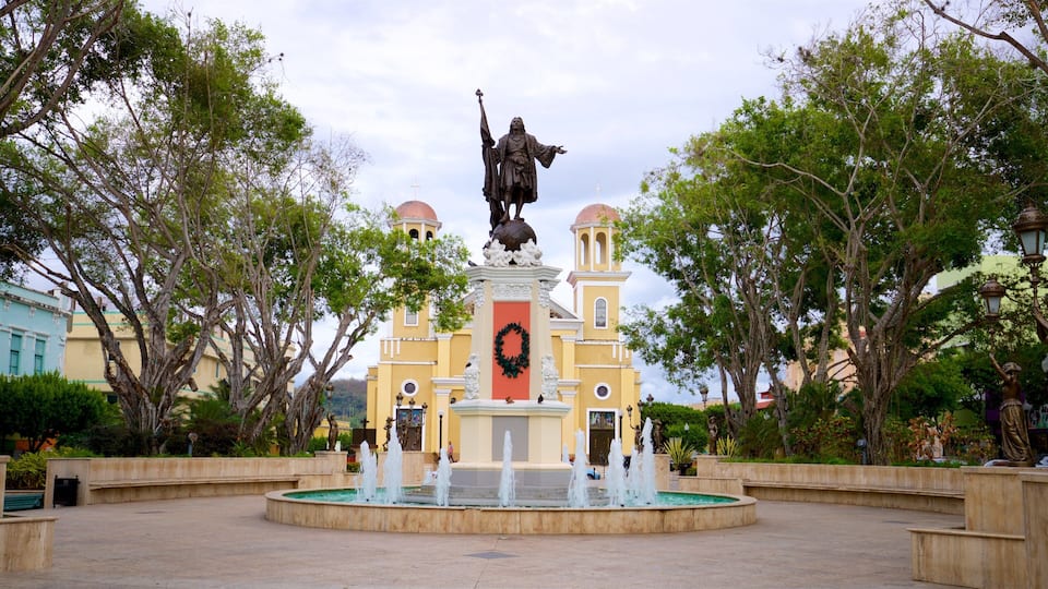 A fountain with a statue in the center, surrounded by trees and buildings.