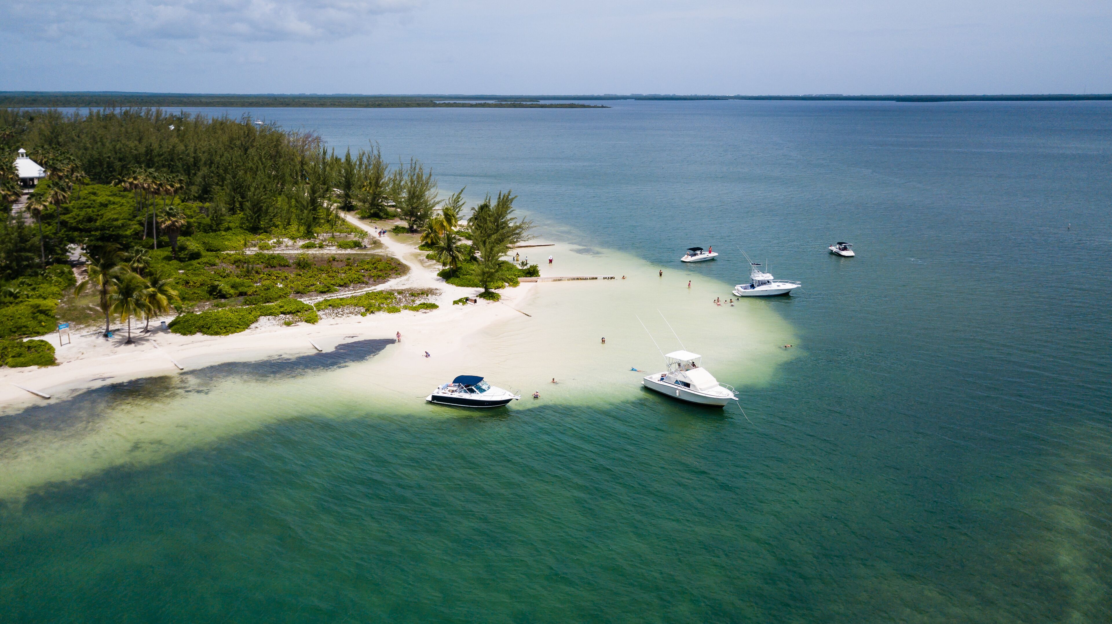 A tropical beach with clear turquoise waters, white sand, and several anchored boats.