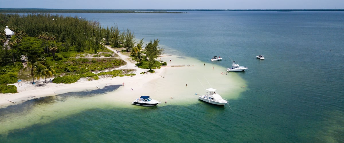 A tropical beach with clear turquoise waters, white sand, and several anchored boats.