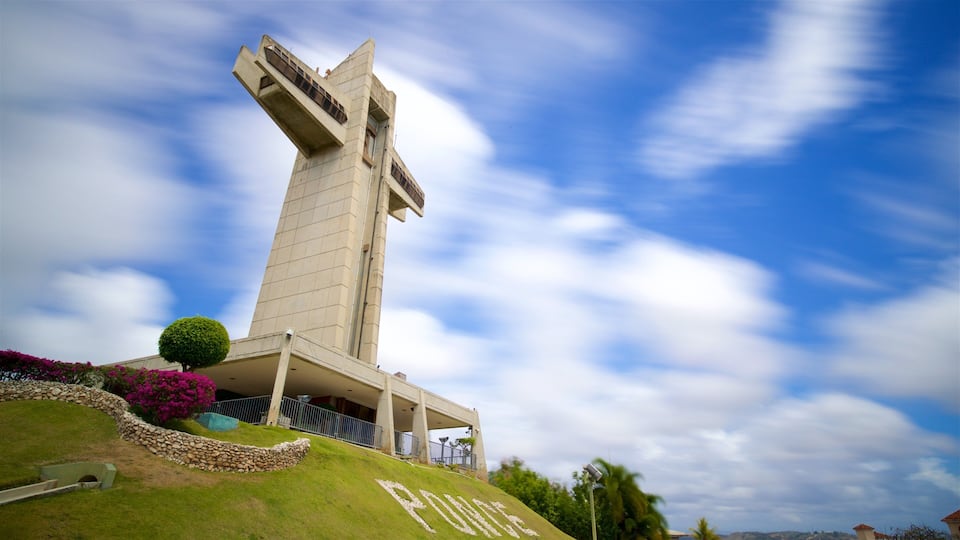 A tall, modern building with a unique design, surrounded by a well-maintained garden and a clear blue sky.