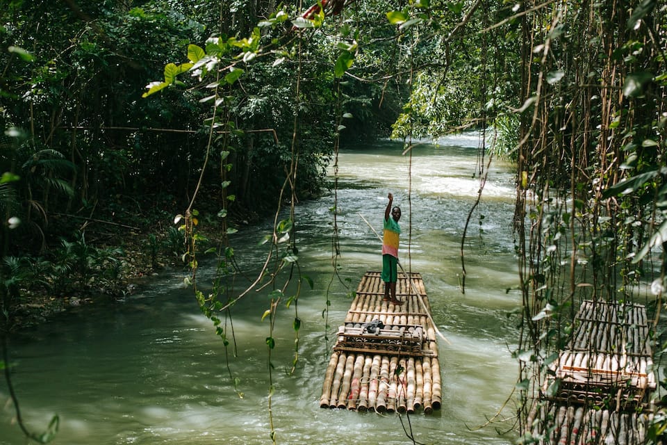 A river with a person standing on a bamboo raft.