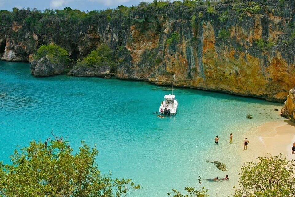Mar turquesa amb vaixells, una platja sorrenca i penya-segades rocoses.