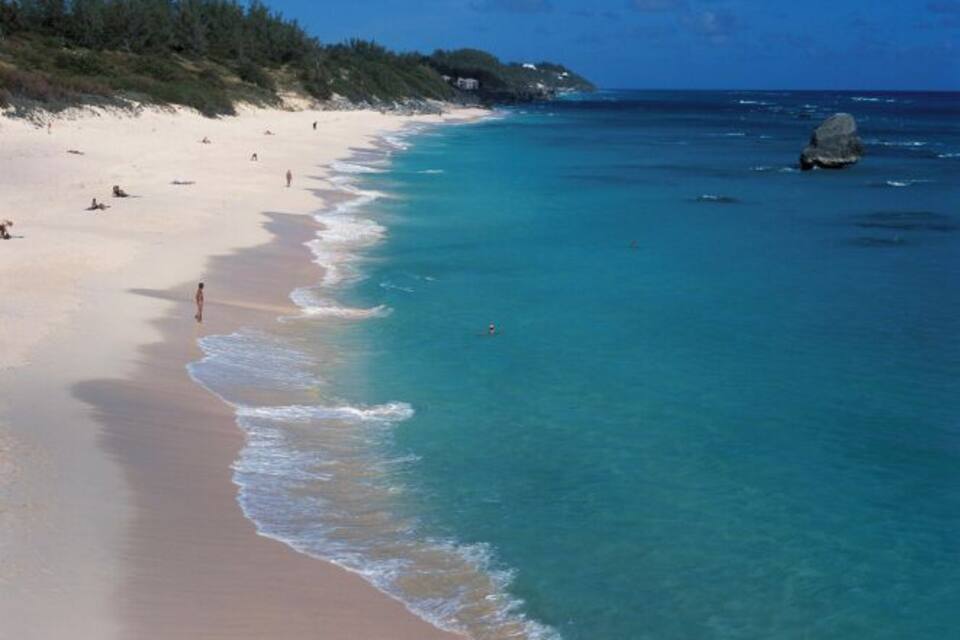 A beach with clear turquoise water, sandy shore, and a rocky outcrop.