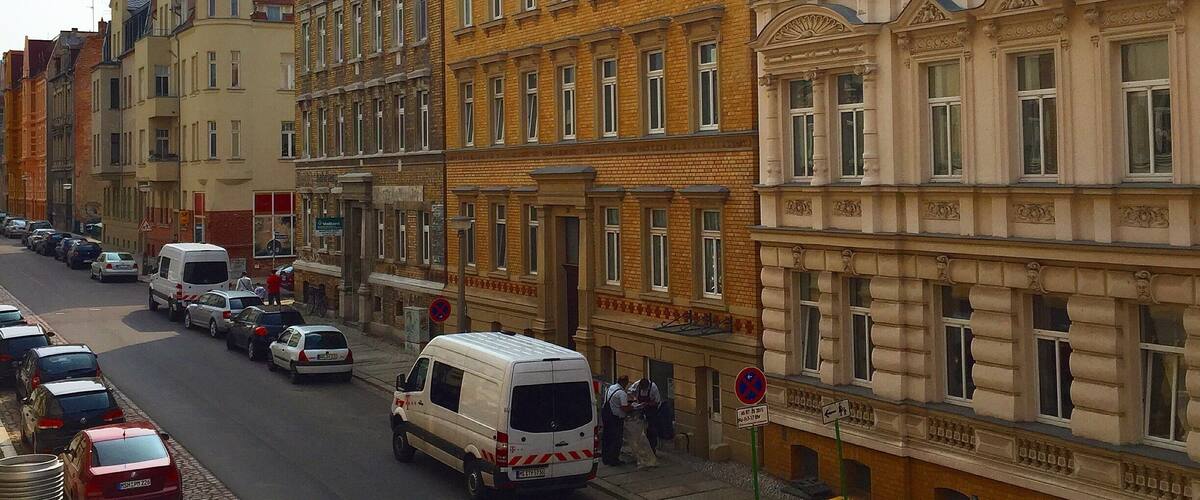 A street lined with multi-story buildings, parked cars, and a white van.