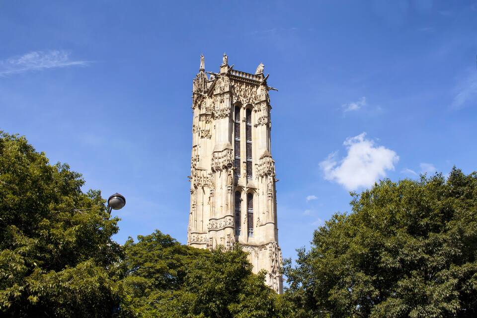 A tall, ornate tower with intricate carvings, surrounded by lush green trees.