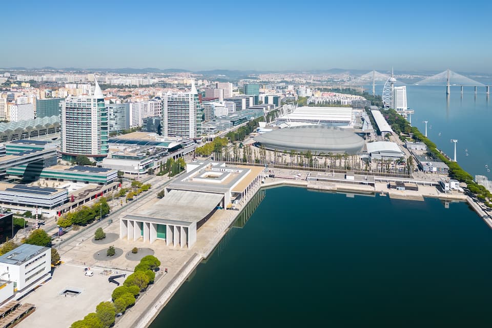 A cityscape with modern buildings, a large stadium, and a bridge over a body of water.