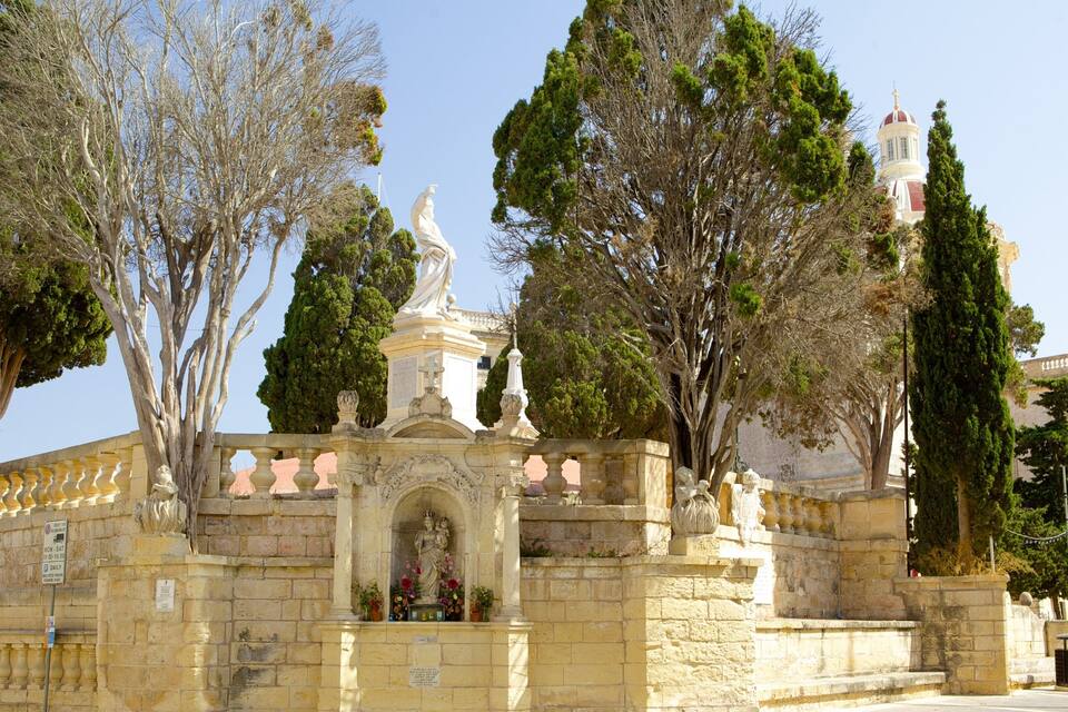 Edifici de pedra històric amb estàtues, envoltat d'arbres i un edifici amb cúpula.