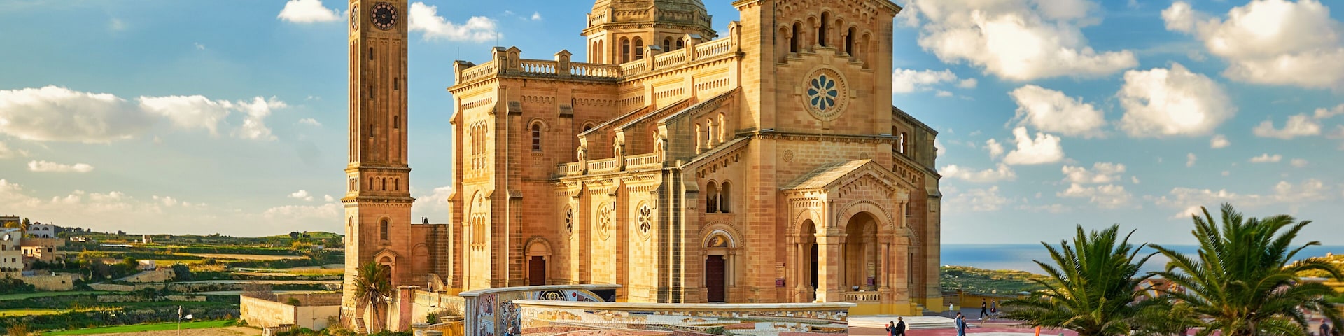 A historic church with a prominent tower and dome, set against a clear sky with scattered clouds.