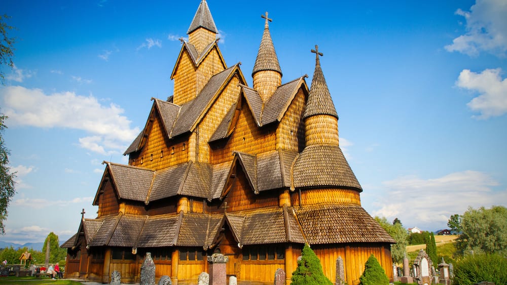 Eine Holzkirche mit mehreren Kirchtürmen und Kreuzen, umgeben von einem Friedhof mit Grabsteinen.