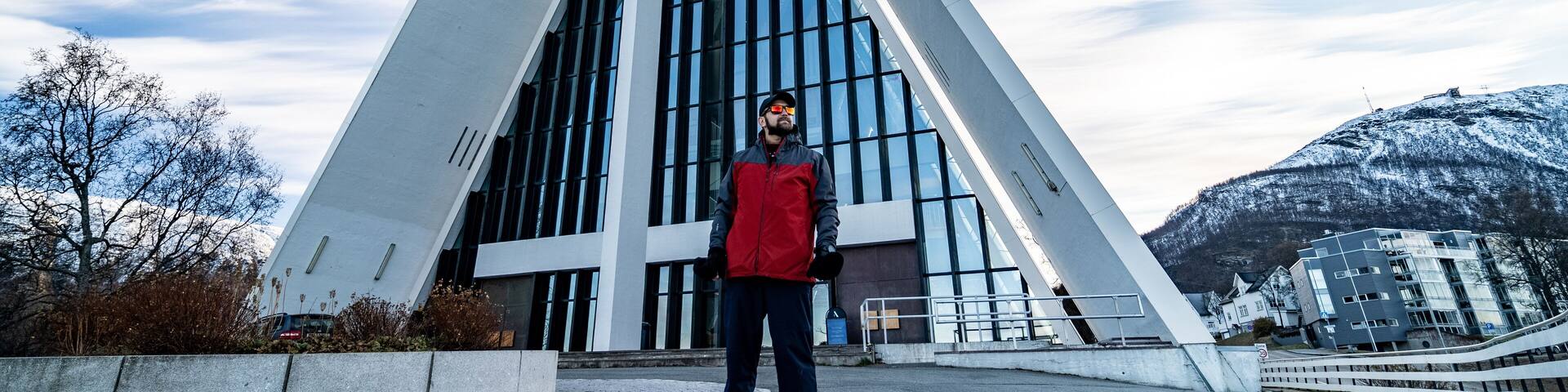 young man with beard stands in front of arctic cathedral in tromso, norway