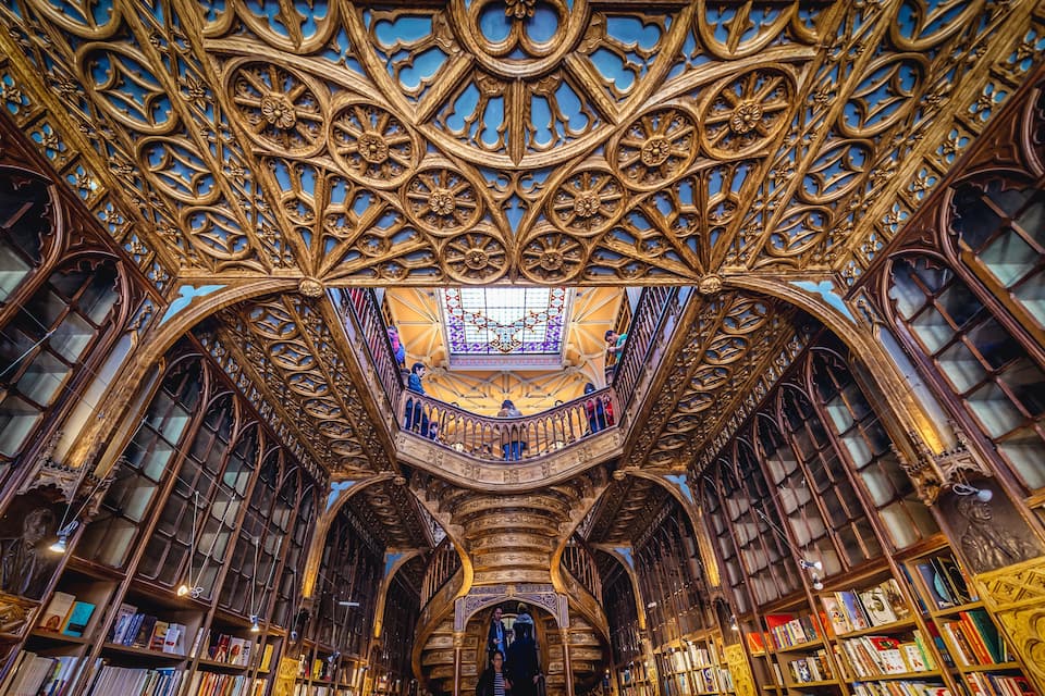 Interior de biblioteca ornamentada, com detalhes elaborados em madeira e uma escadaria central.