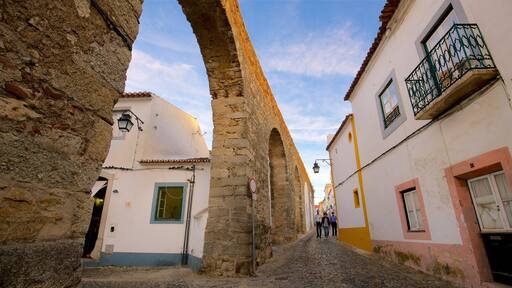 Una calle empedrada bordeada por edificios históricos de piedra con puertas arqueadas y un cielo azul despejado.